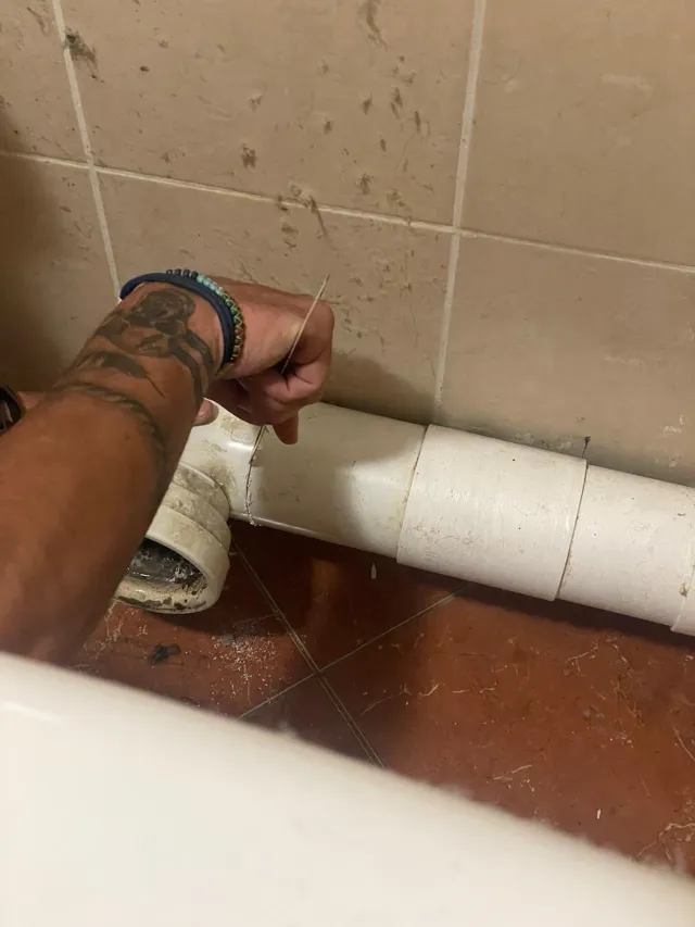 Découpe d'un tuyau d'évacuation en PVC le long du mur